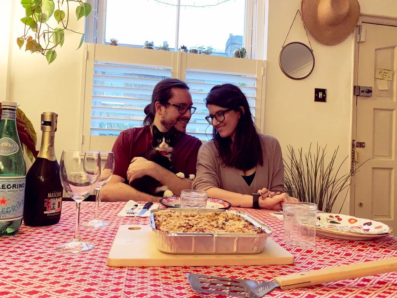 a photo of me and Flavia, I hold Jessy, a tuxedo cat in my arms. On the table there&#x27;s a bottle of prosecco, glasses and a hole pan of lasagna